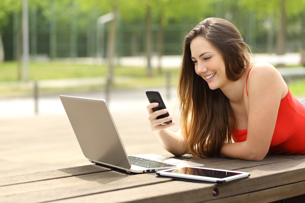 Girl using a laptop and smart phone in a park