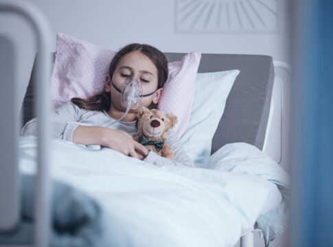Sick girl with oxygen mask sleeping in a hospital bed with teddy