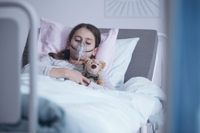Sick girl with oxygen mask sleeping in a hospital bed with teddy
